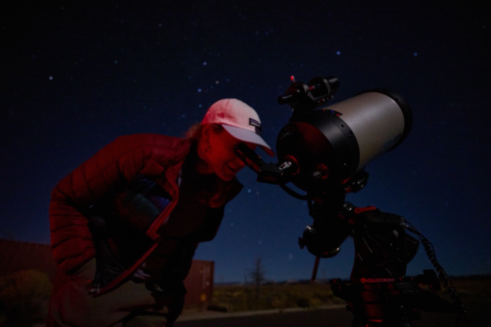 Photographer wearing a red headlamp working at a Celestron telescope eyepiece under a starry night sky near Bryce Canyon