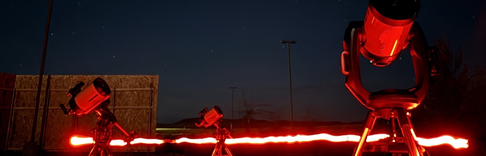 Row of telescopes set up at dusk with a red light streak across the foreground before a stargazing tour